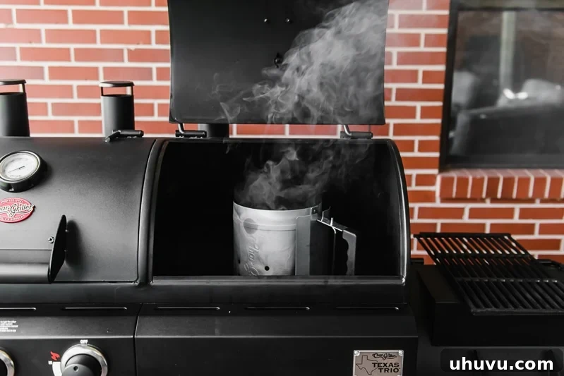 A chimney starter filled with charcoal actively smoking and igniting, indicating it's heating up properly.