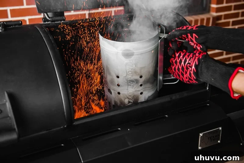 Glowing, ash-covered charcoal being carefully dumped from a chimney starter into a grill.
