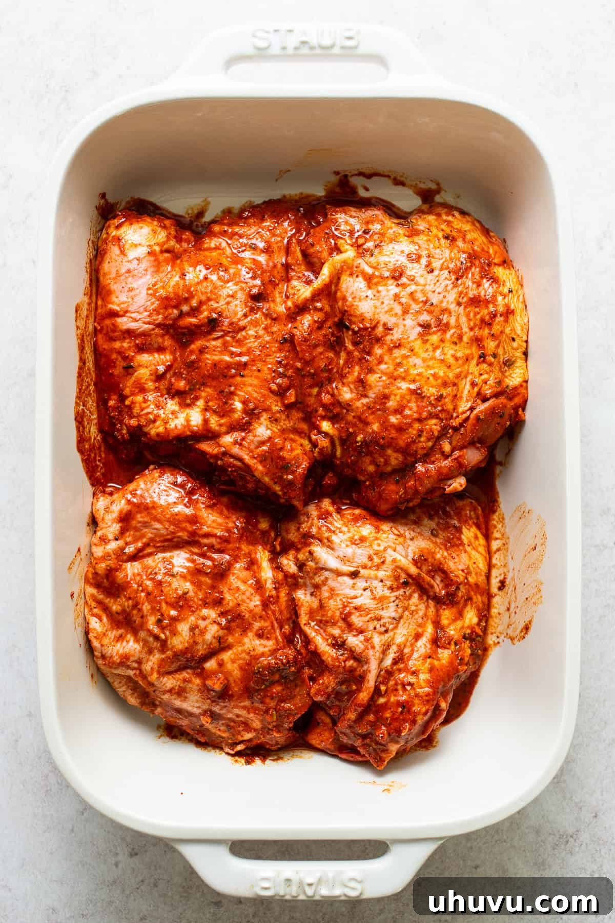 Flavorful Roasted Chicken 4 Chicken pieces marinating in a vibrant red-orange sauce within a baking dish, ready for cooking.