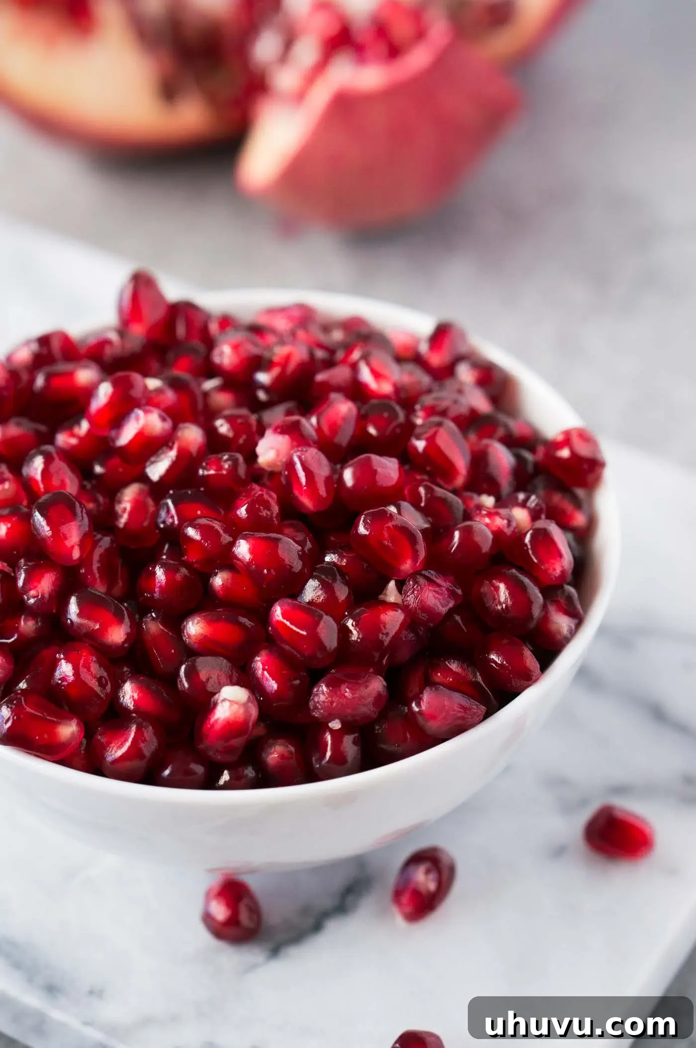 Close-up of fresh, juicy pomegranate arils in a white bowl, glistening and ready to be enjoyed.