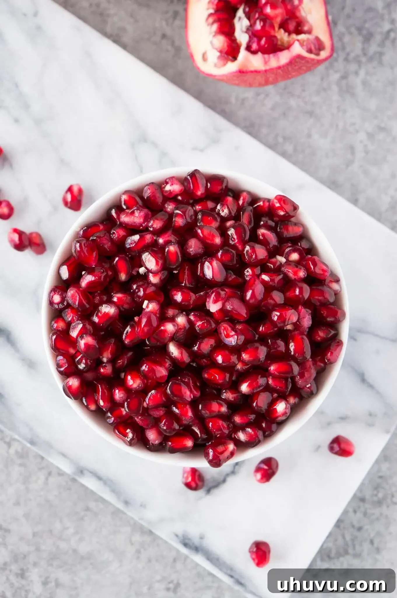 Overhead view of fresh pomegranate arils in a white bowl, glistening with juice.