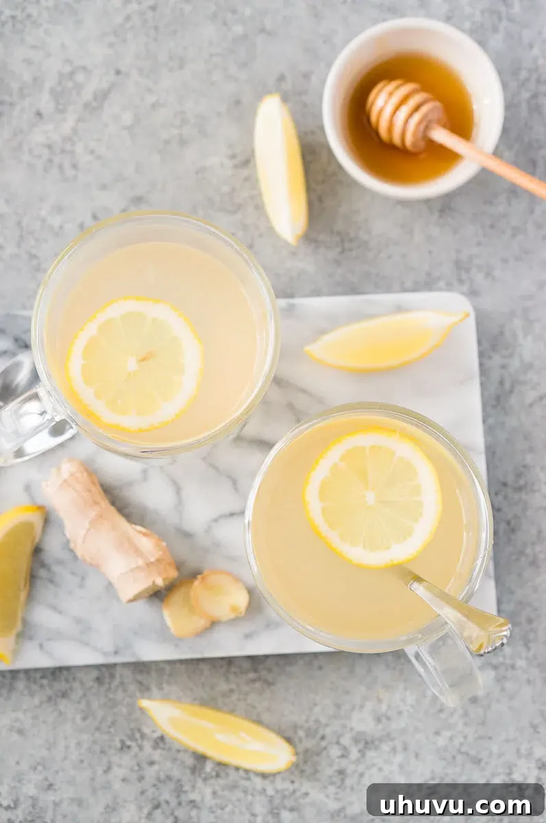 Two glass mugs of honey ginger tea with slices of lemon and fresh ginger on a white background.