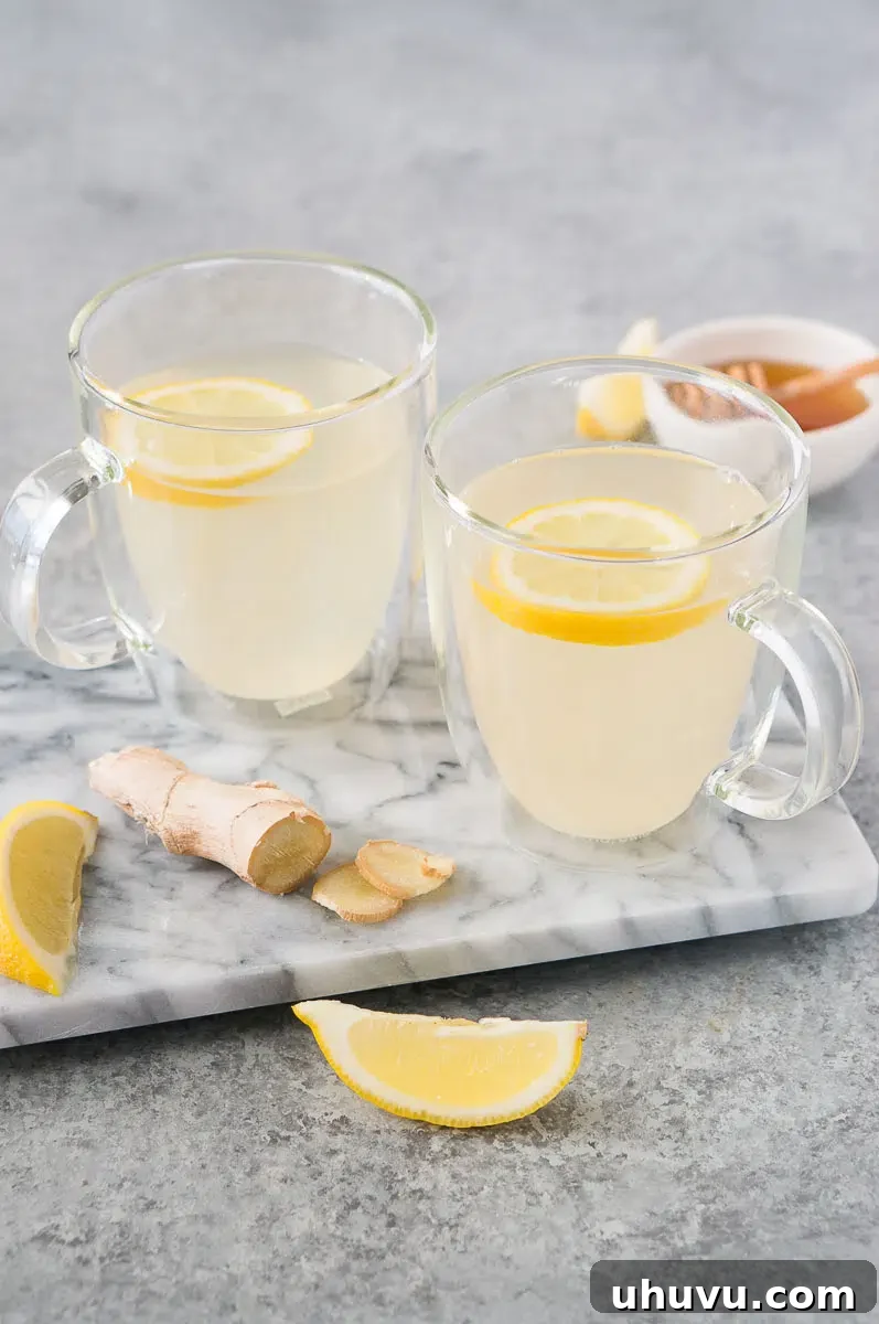 Two aesthetically arranged cups of lemon ginger tea with lemon and ginger slices on a dark wooden board.