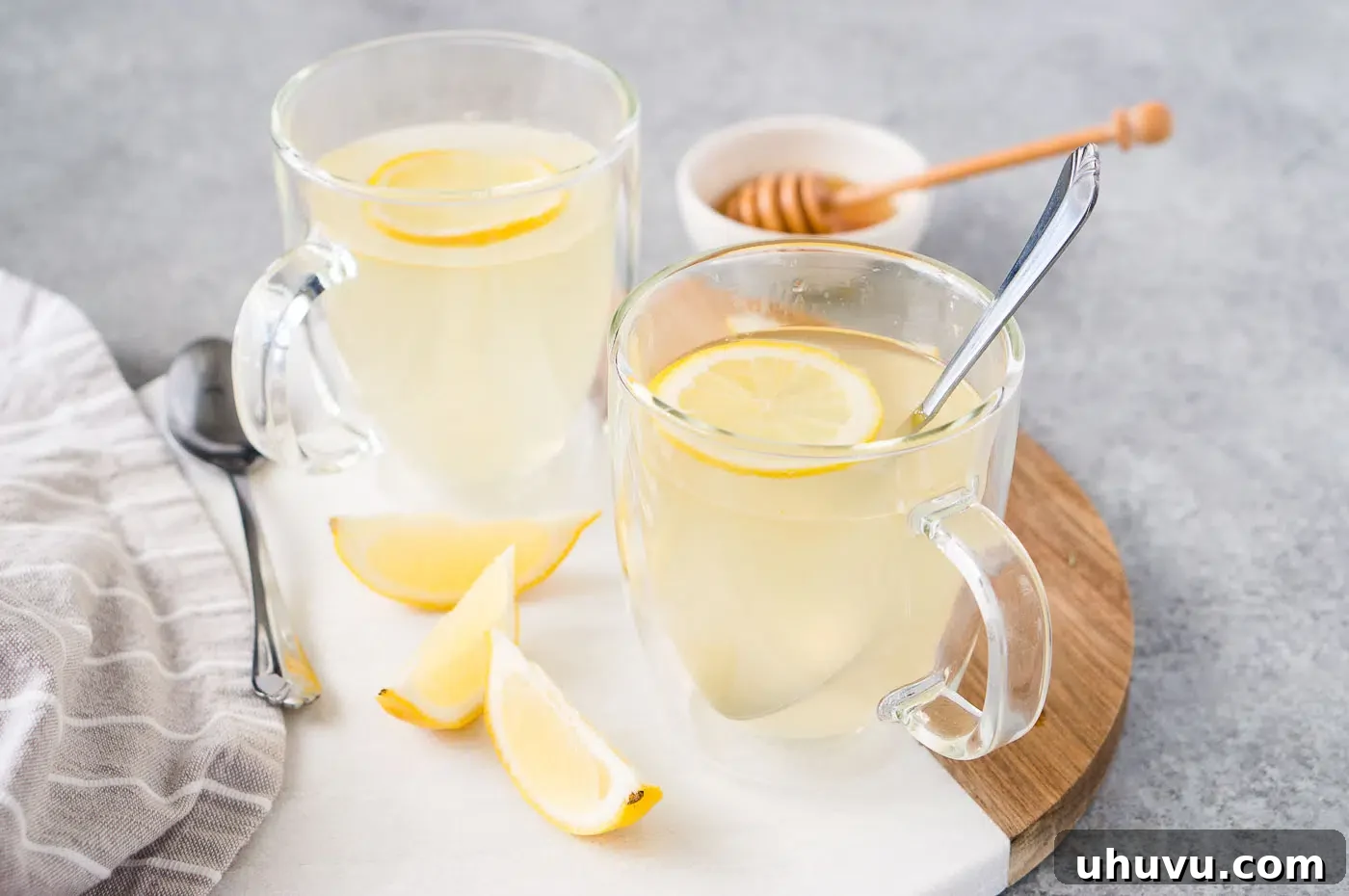 Two clear glass cups of honey lemon tea, garnished with fresh lemon slices.