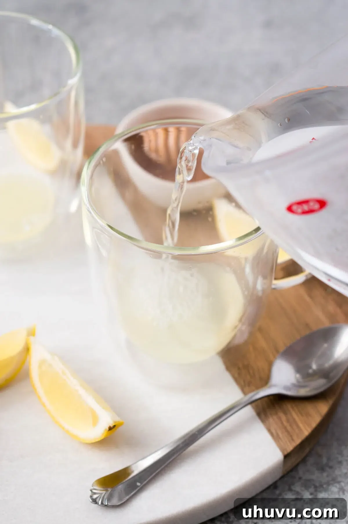 Warm water being poured into a glass cup containing fresh lemon juice.