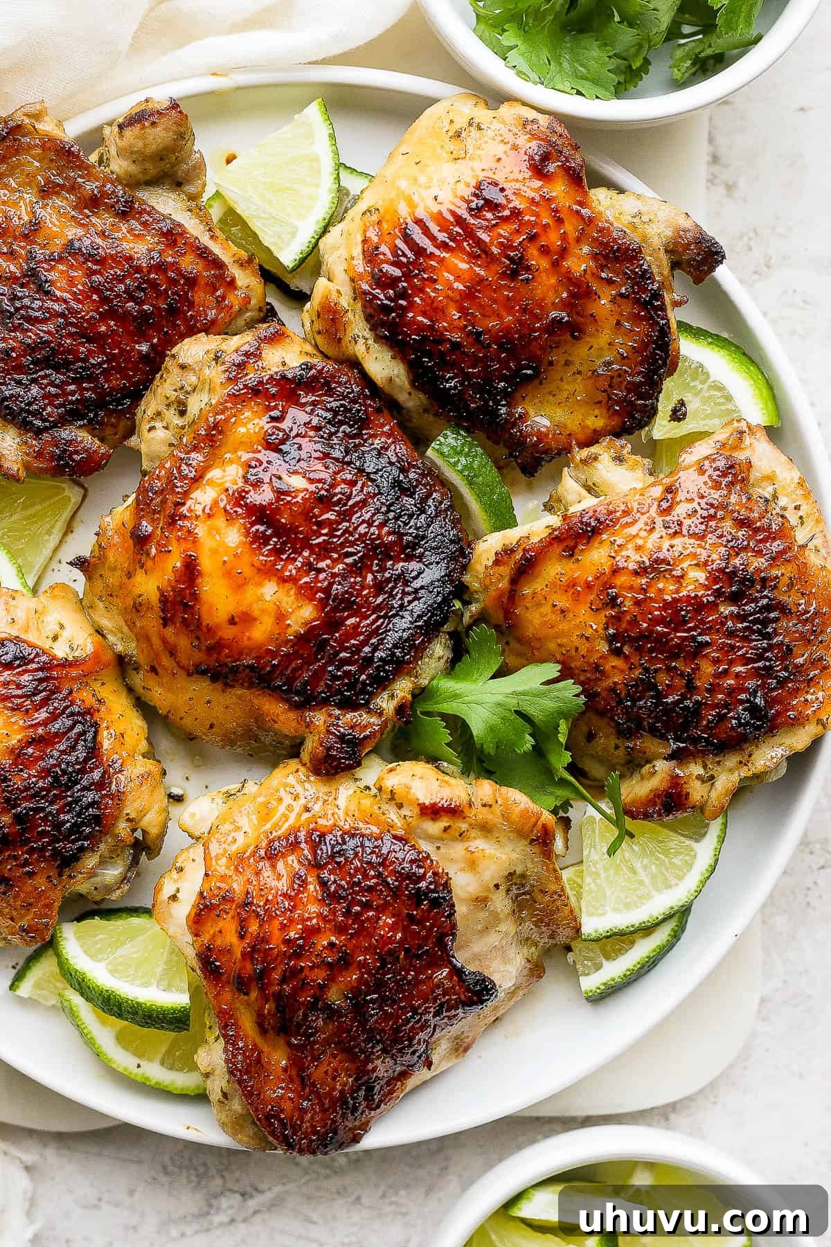 Zesty Cilantro Lime Chicken 2 Golden-brown, crispy-skinned cilantro lime chicken thighs on a white plate, garnished with fresh cilantro and lime wedges.