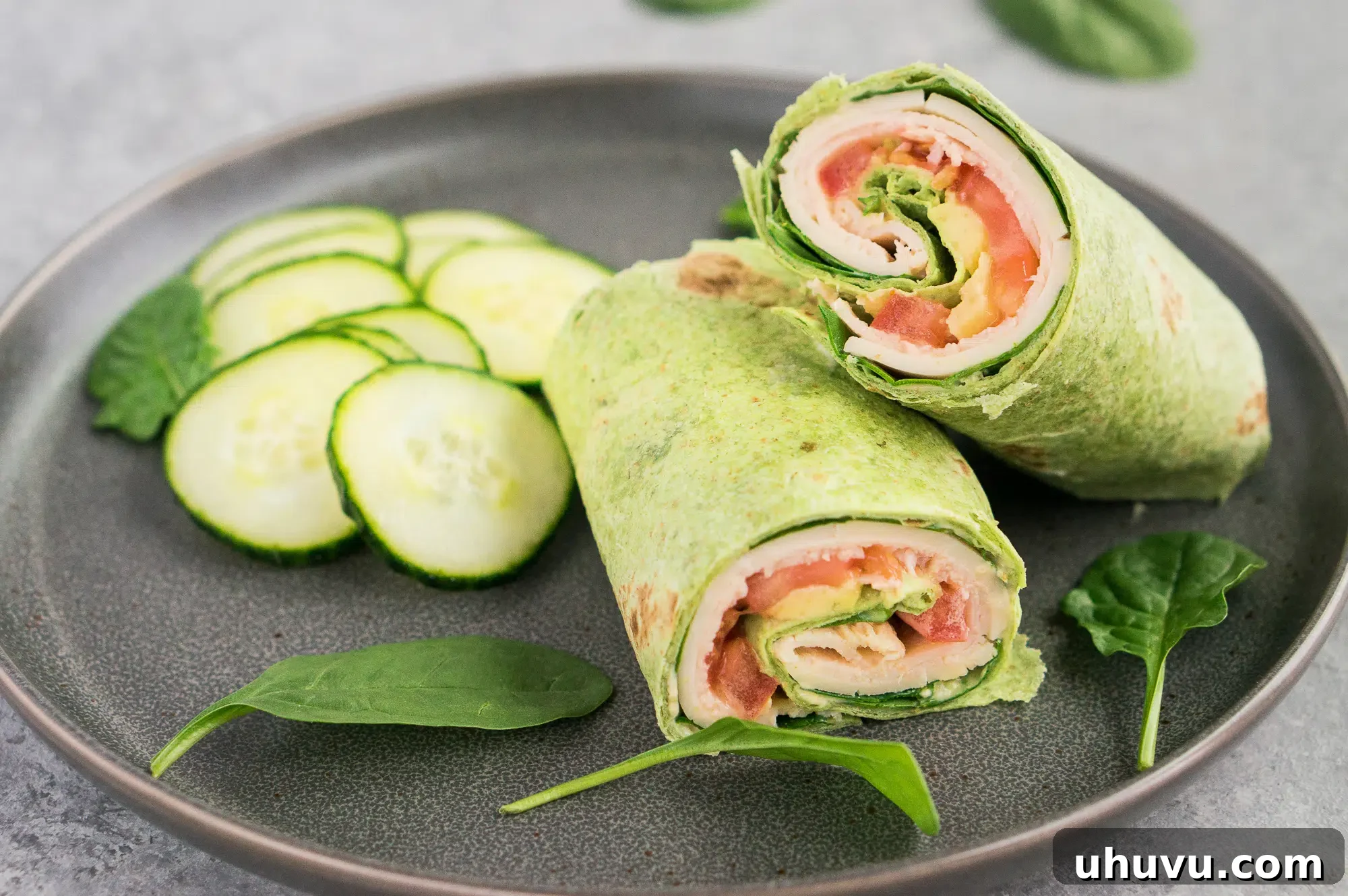 Sliced turkey club wrap with fresh cucumber on a white plate