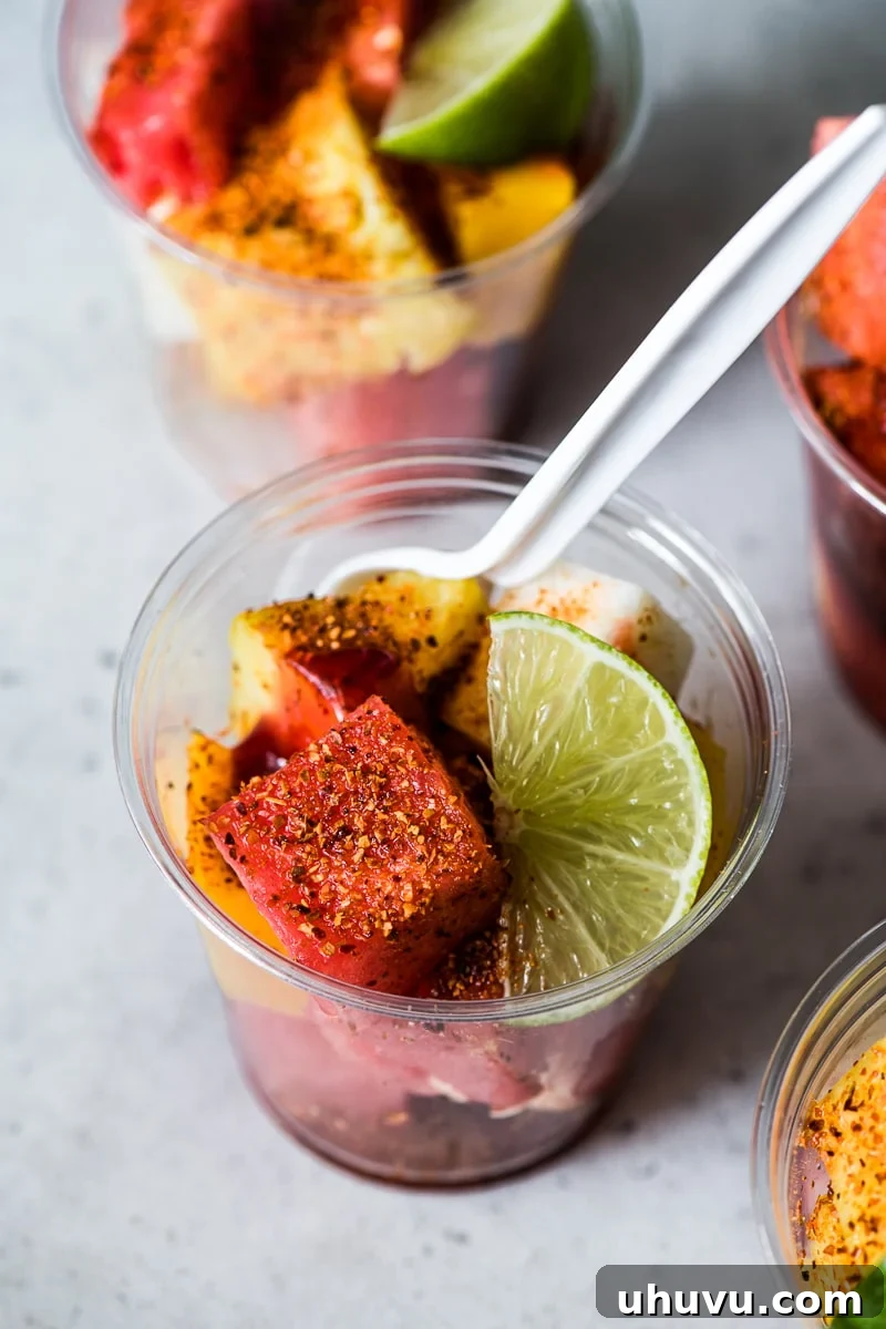 Chili-Lime Fruit Cups 5 Watermelon in a Mexican fruit cup topped with a generous sprinkle of chile lime Tajin seasoning, a drizzle of chamoy sauce, and a fresh lime wedge.