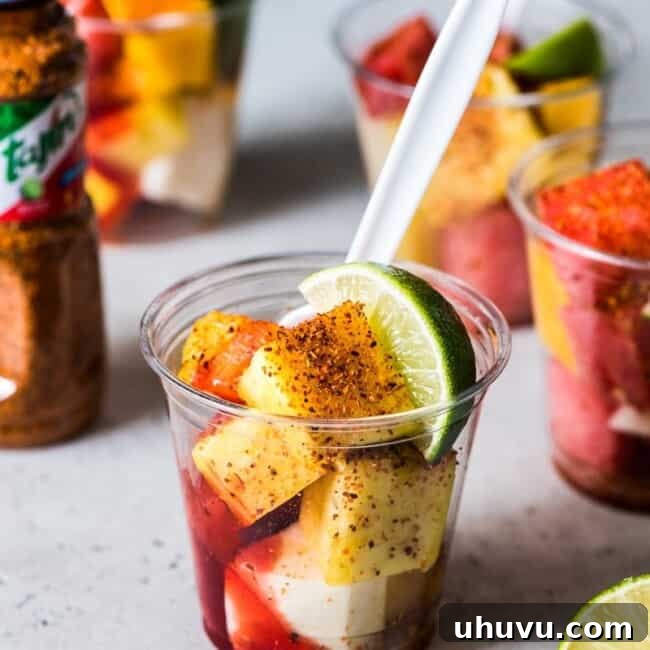 Chili-Lime Fruit Cups 6 Mexican Fruit Cups on a table topped with chile lime seasoning, chamoy and a lime wedge.