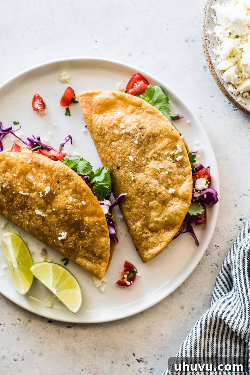 A plate of two crispy potato tacos, garnished with limes and ready to be served.