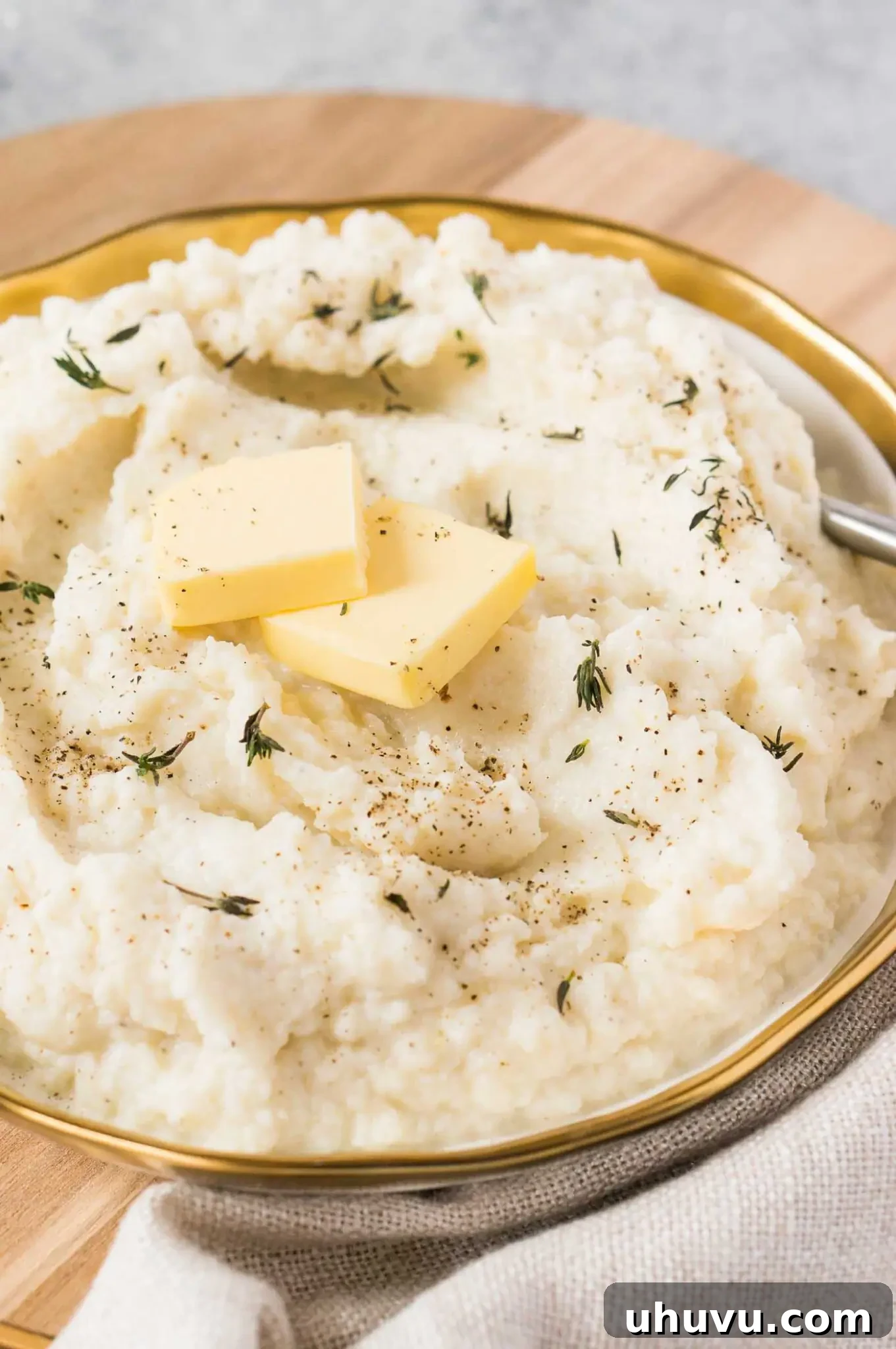 The best mashed cauliflower with butter and garlic in a white bowl, garnished with chives.