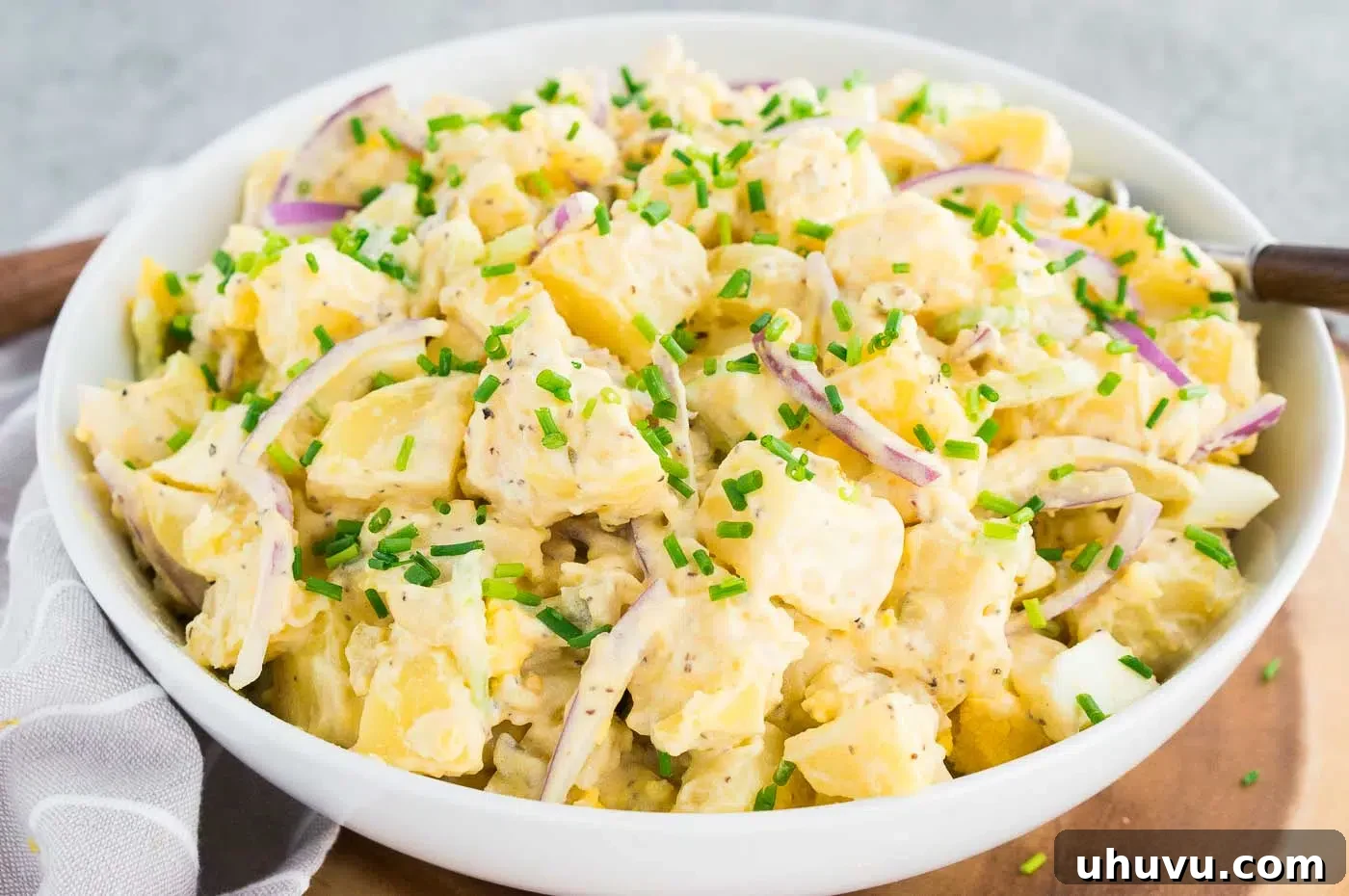 Close-up shot of a classic potato salad with a creamy dressing and visible potato chunks, celery, and egg pieces, served in a white bowl.