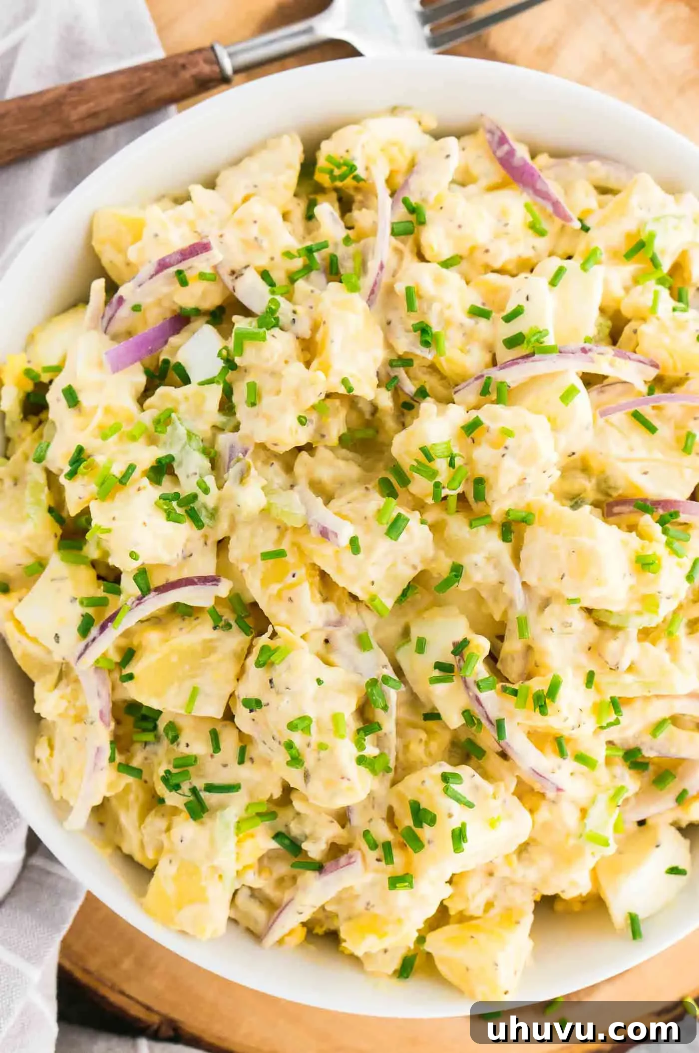 A close-up of quick and easy potato salad in a white bowl with a fork, showing its creamy texture and fresh ingredients.