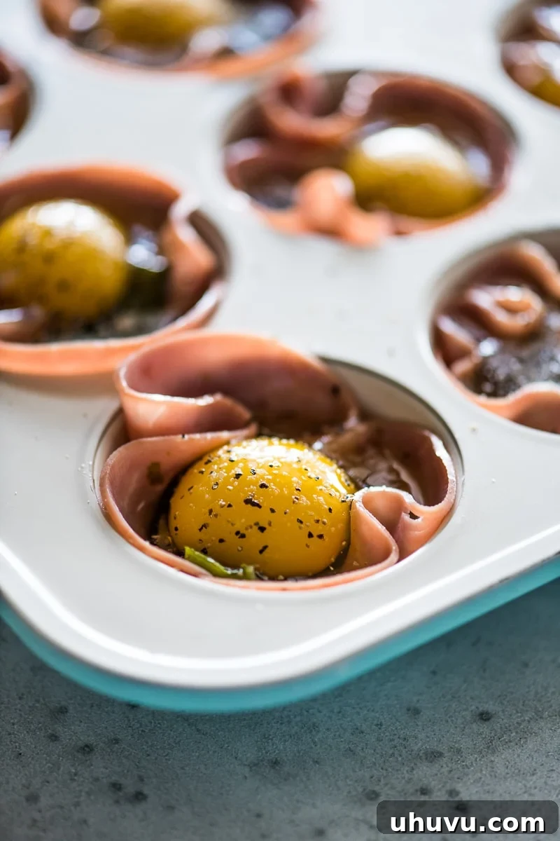 Poblano and Ham Egg Bake 4 A cracked egg with the yolk in an egg muffin cup topped with black pepper and salt.