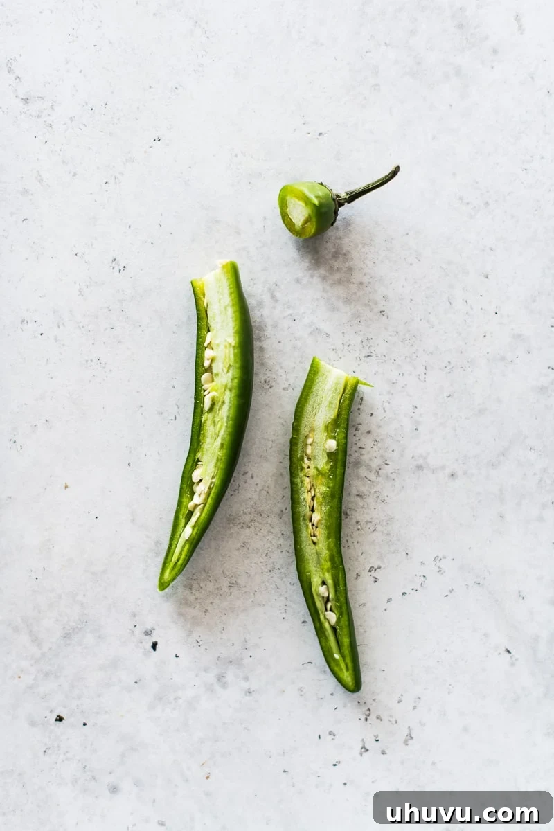 Decoding Serrano Peppers 5 A Serrano pepper cut cleanly in half lengthwise, revealing the internal structure of bright white veins and numerous small seeds, which are the primary source of the pepper's heat.