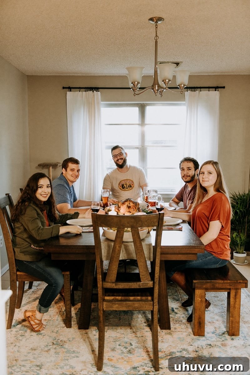 Friendsgiving Fun: Tips, Tricks, and Treats 12 Smiling friends gathered around the dinner table, enjoying their Friendsgiving meal together.