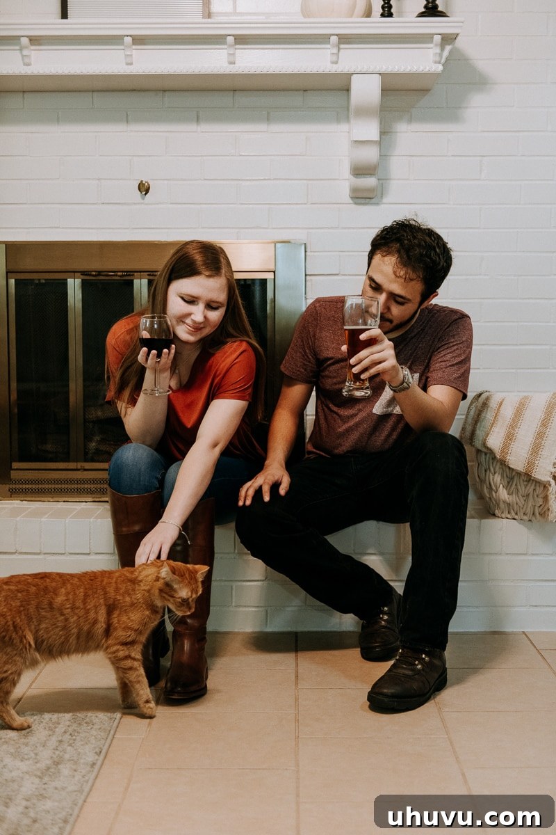 Friendsgiving Fun: Tips, Tricks, and Treats 6 A couple relaxing by the fireplace, petting a cat and enjoying the warm ambiance of their Friendsgiving celebration.