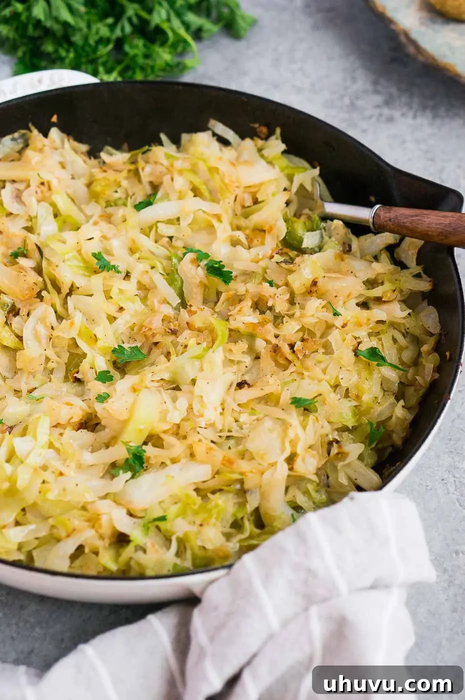 Sauteed cabbage served in a white skillet, garnished with fresh parsley.