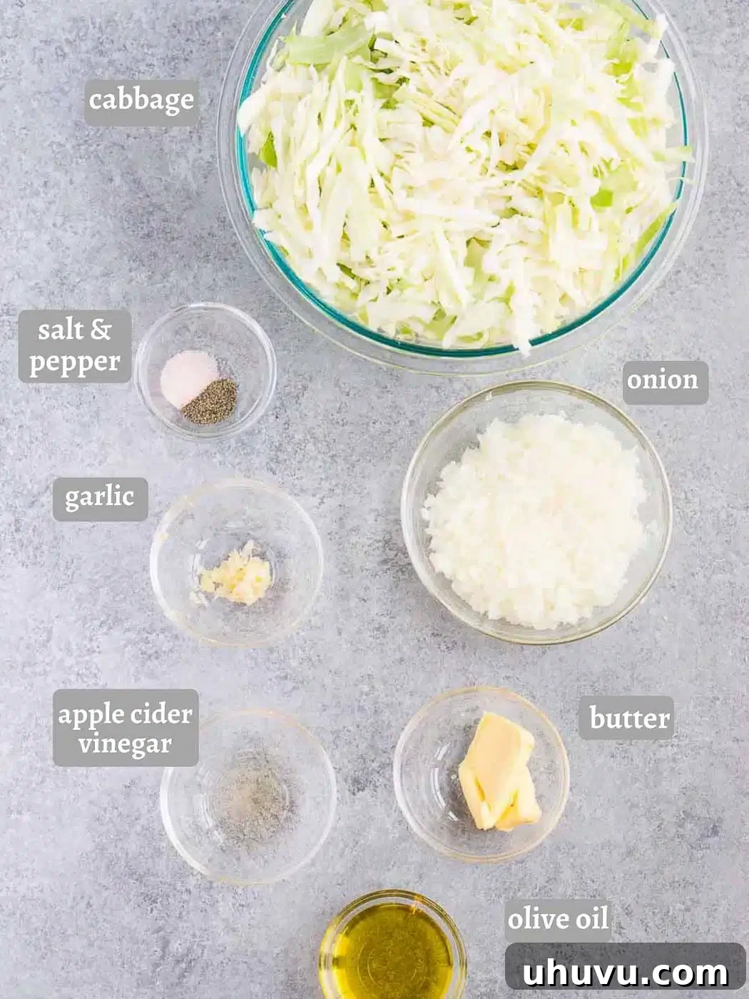 Fresh ingredients laid out on a wooden cutting board: shredded cabbage, a whole onion, garlic cloves, olive oil, and butter.