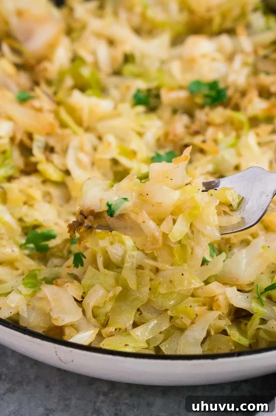 A fork holding a bite of sautéed cabbage, showing its tender texture and golden color.