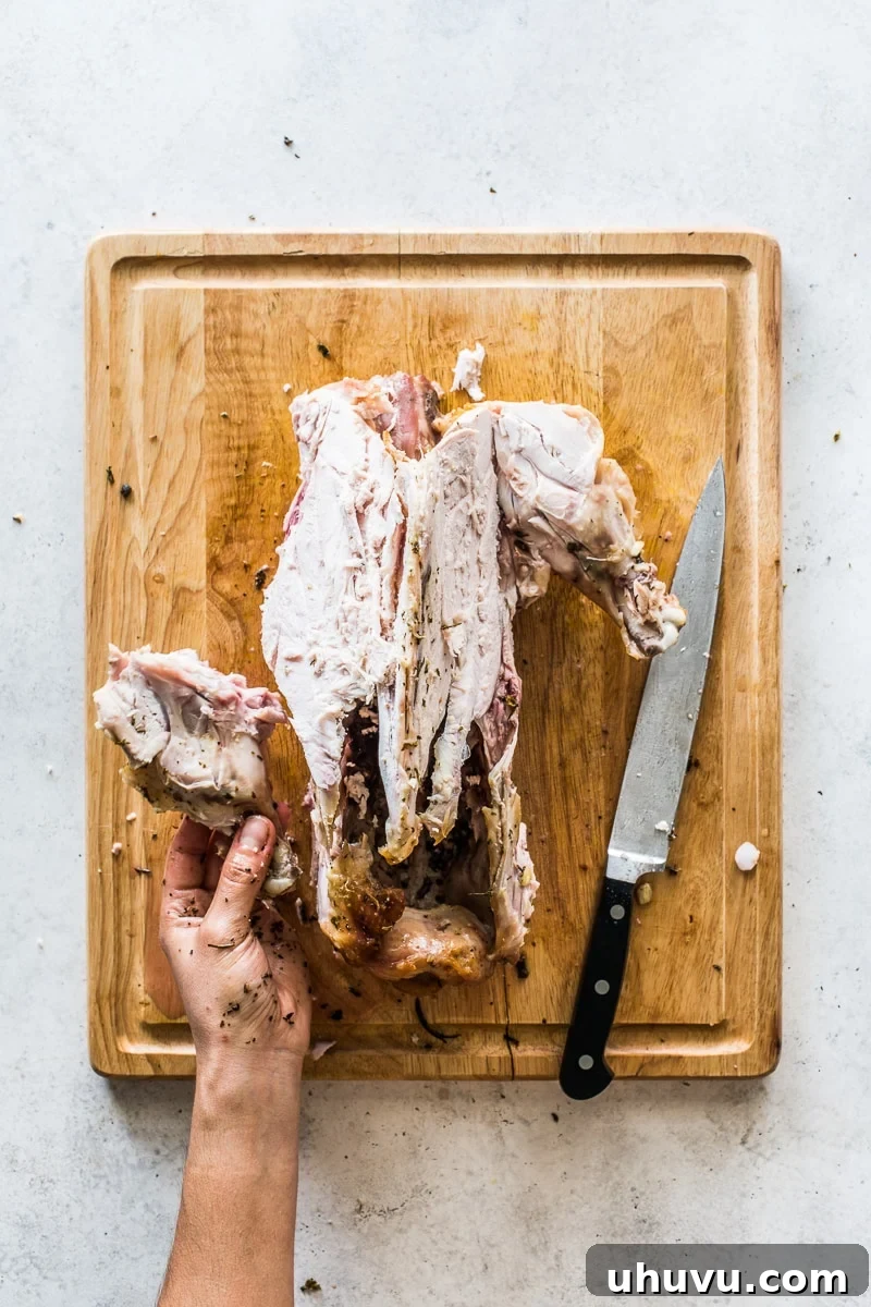 Carefully carving the drumette wing from the turkey carcass after the breast has been removed, highlighting a clean separation at the joint.