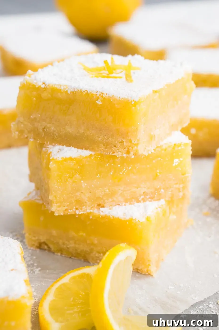 Stacked lemon bars and lemon slices on a board, dusted with powdered sugar