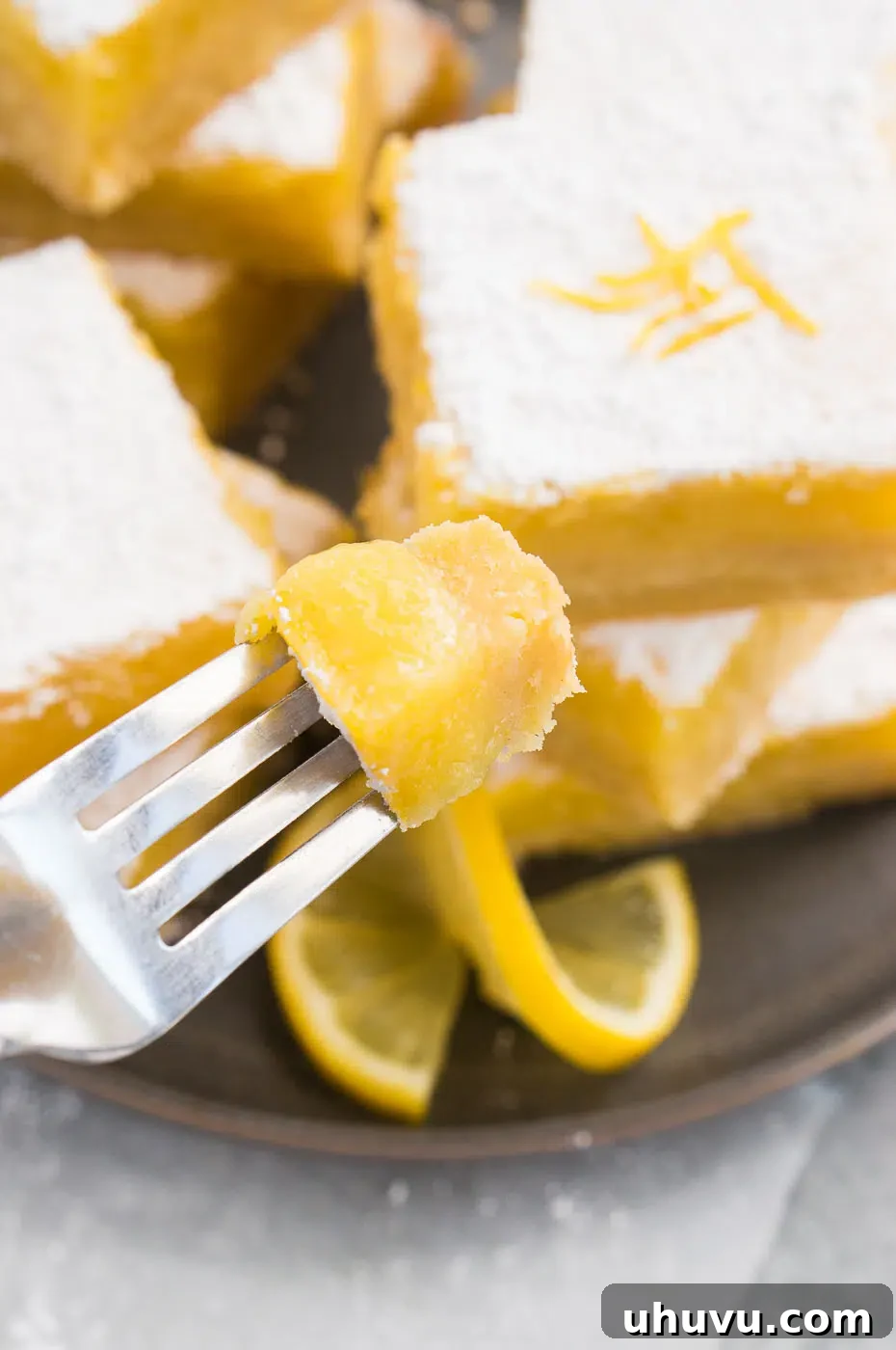 A close-up of a lemon bar with a bite taken out, showing the layers of crust and curd