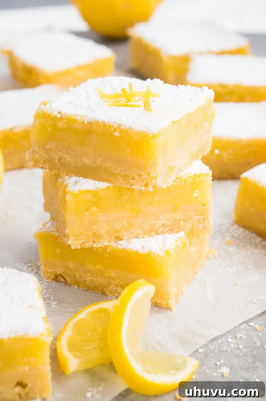 Sliced lemon squares and a lemon slice on parchment paper, ready to be served