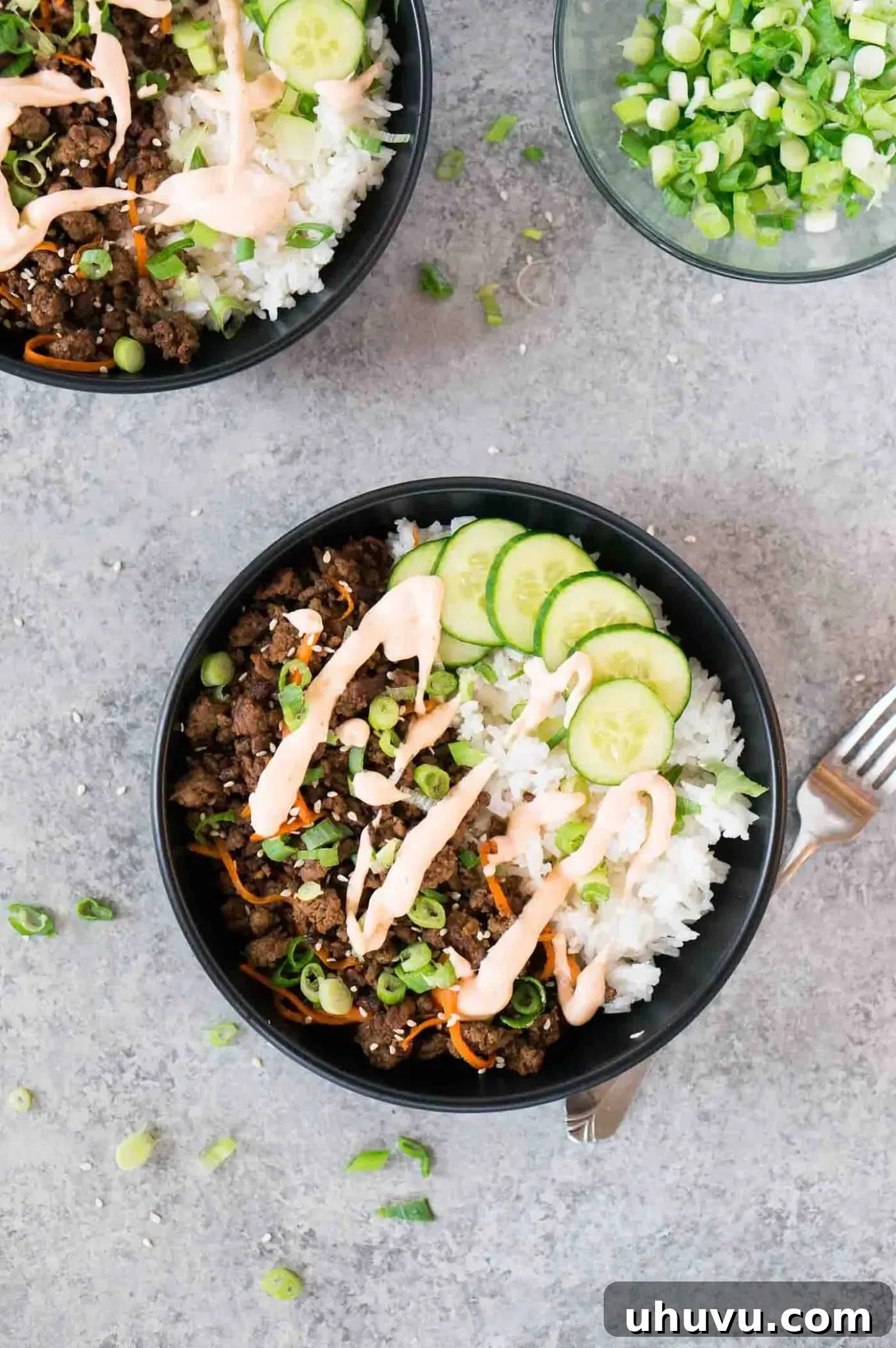 Two Korean beef bowls with sriracha mayo, rice, and fresh garnishes, ready to eat