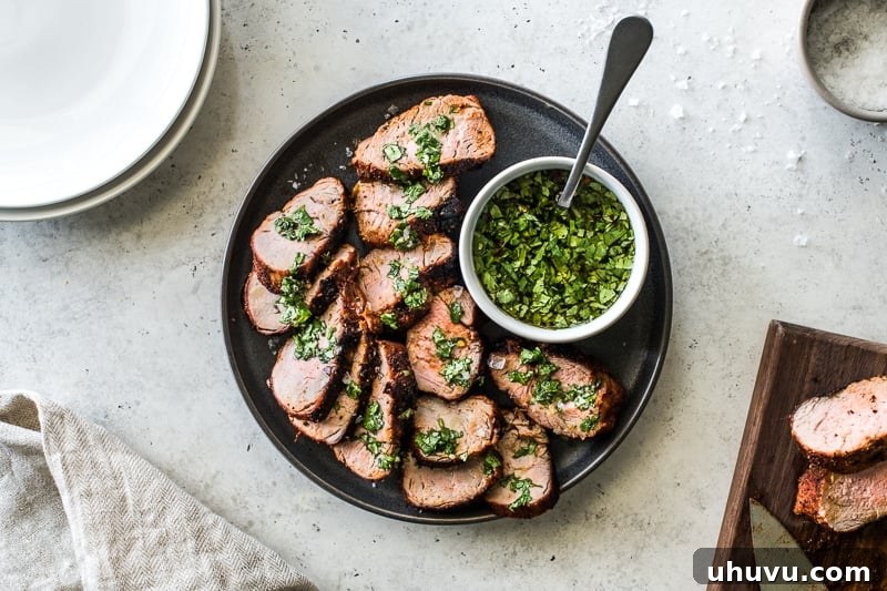 Grilled pork tenderloin slices on a plate topped with a green herb sauce.