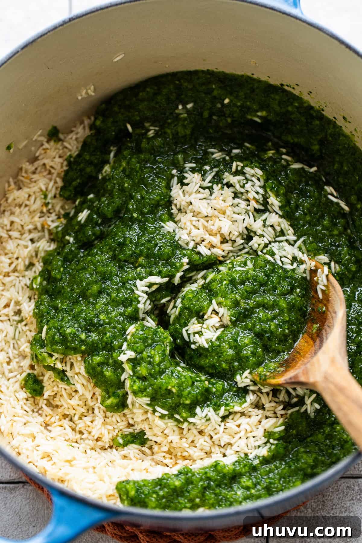 Zesty Green Rice 7 A vibrant green verde mixture, made from blended herbs and peppers, being stirred into a pot of toasted rice.