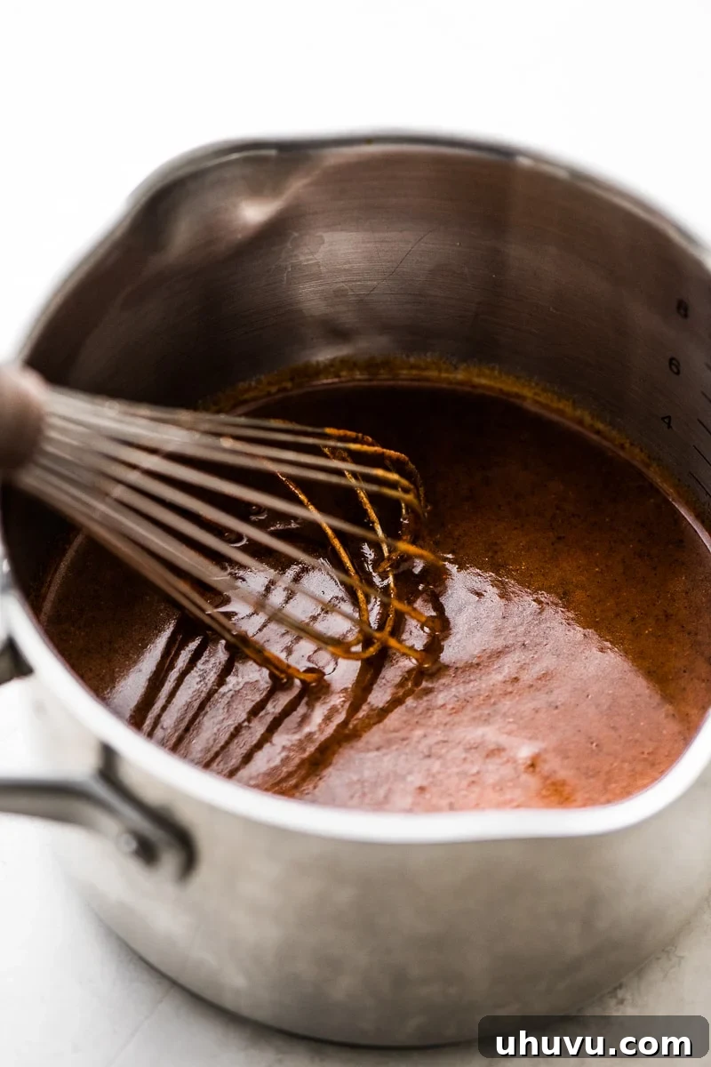 Enchilada sauce simmering in a pot with a whisk during preparation.