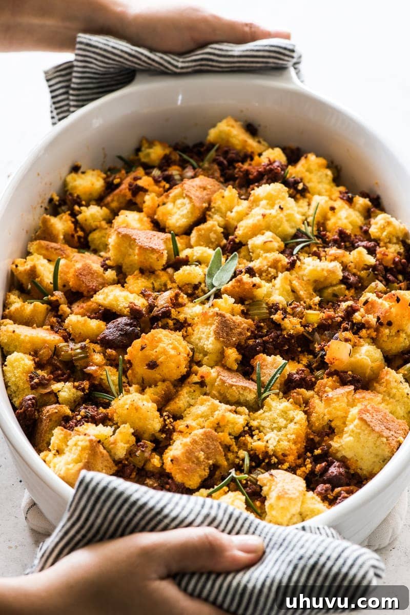 Cornbread stuffing with chorizo in a baking dish topped with fresh sage and rosemary.