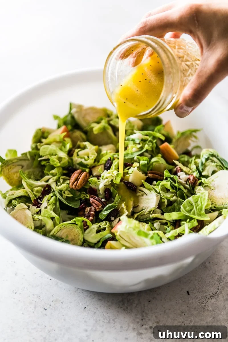 Bright Brussels Sprout Medley 6 A hand pouring the lemon dijon dressing over a bowl of Brussels sprout salad ingredients.