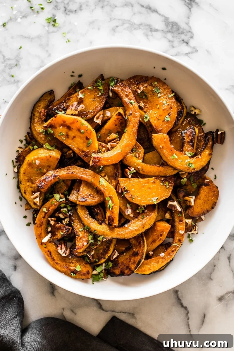 A bowl filled with roasted butternut squash, drizzled with maple-lime sauce and garnished with pecans and cilantro.