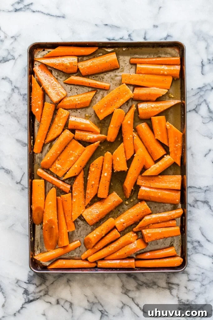 Glazed Maple Cinnamon Carrots 4 Carrots evenly spread in a single layer on a parchment-lined baking sheet before roasting.