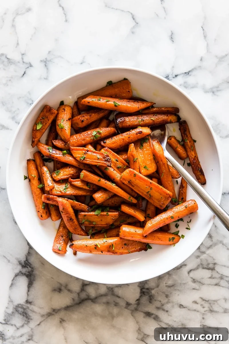 Glazed Maple Cinnamon Carrots 6 Maple glazed roasted carrots scattered with fresh herbs on a white plate, ready to be served.