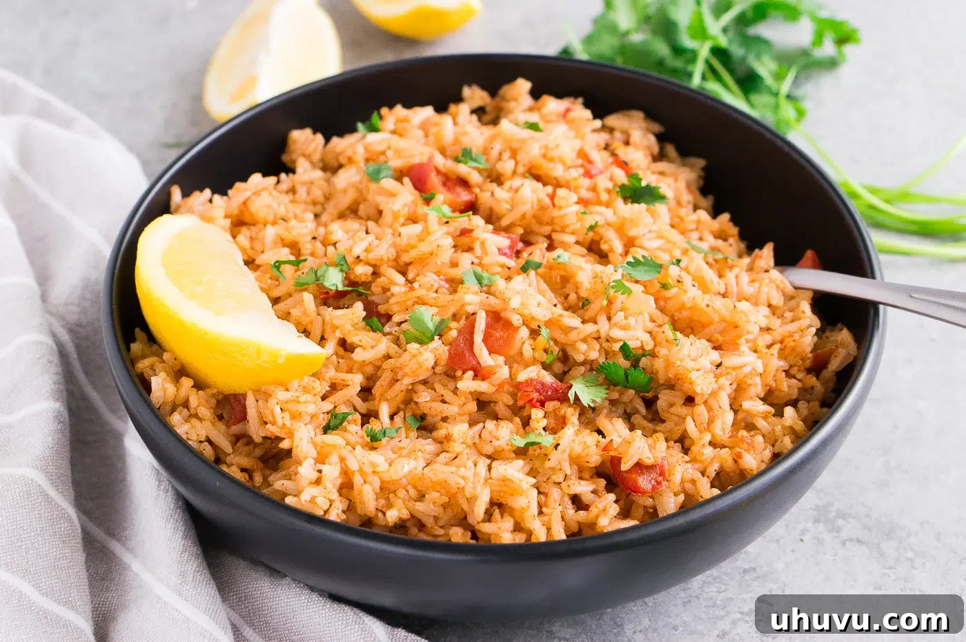 A black bowl filled with perfectly cooked Spanish rice, garnished with a lemon wedge and fresh herbs.