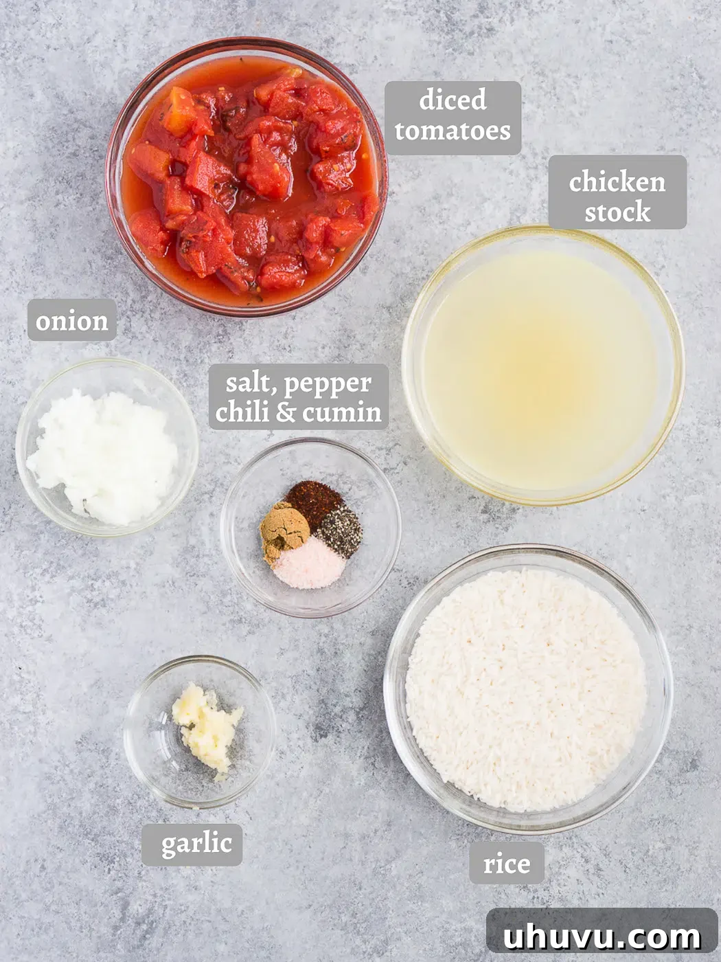 A flat lay of all the ingredients needed to make Spanish rice: olive oil, onion, garlic, rice, stock, spices, and canned tomatoes.