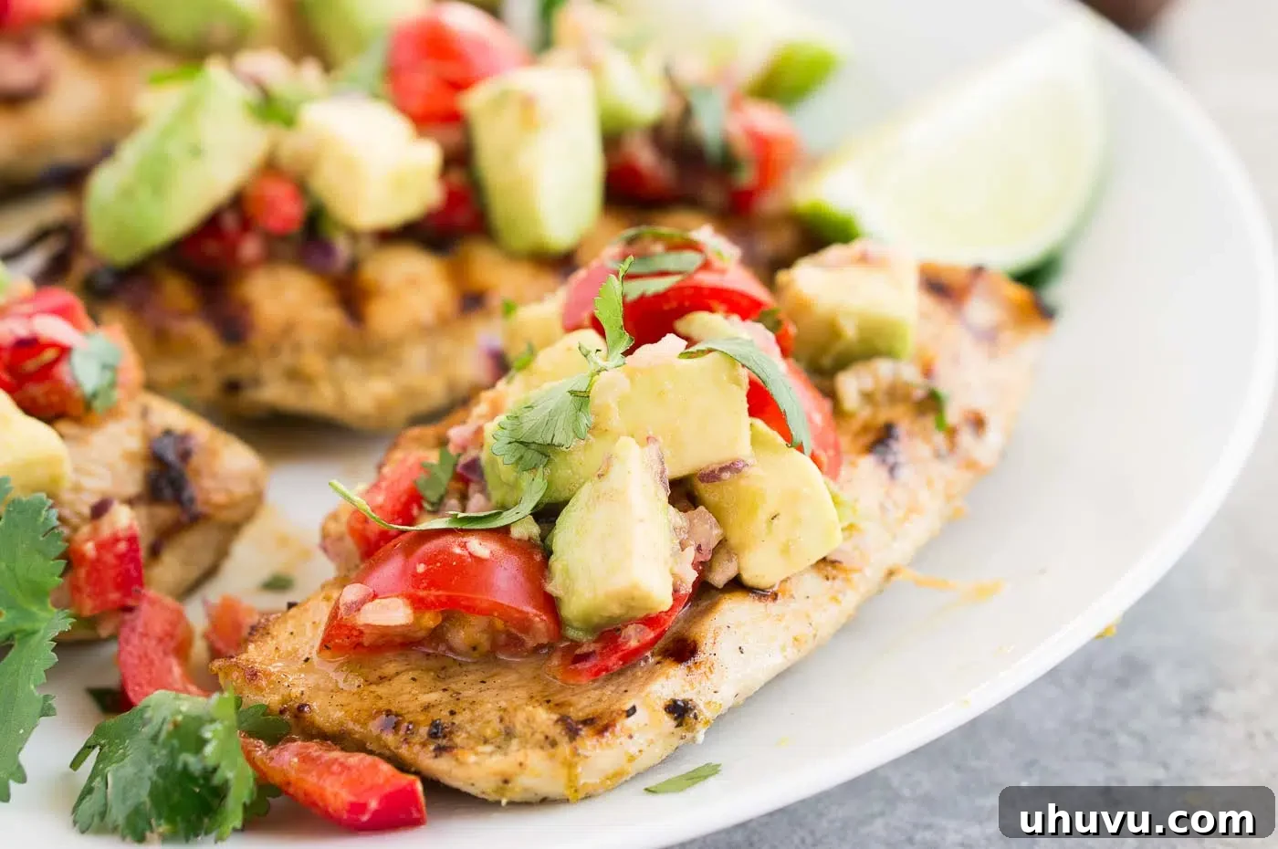 Close-up of succulent cilantro lime marinated chicken, garnished with fresh cilantro and lime wedges, with a side of avocado salsa