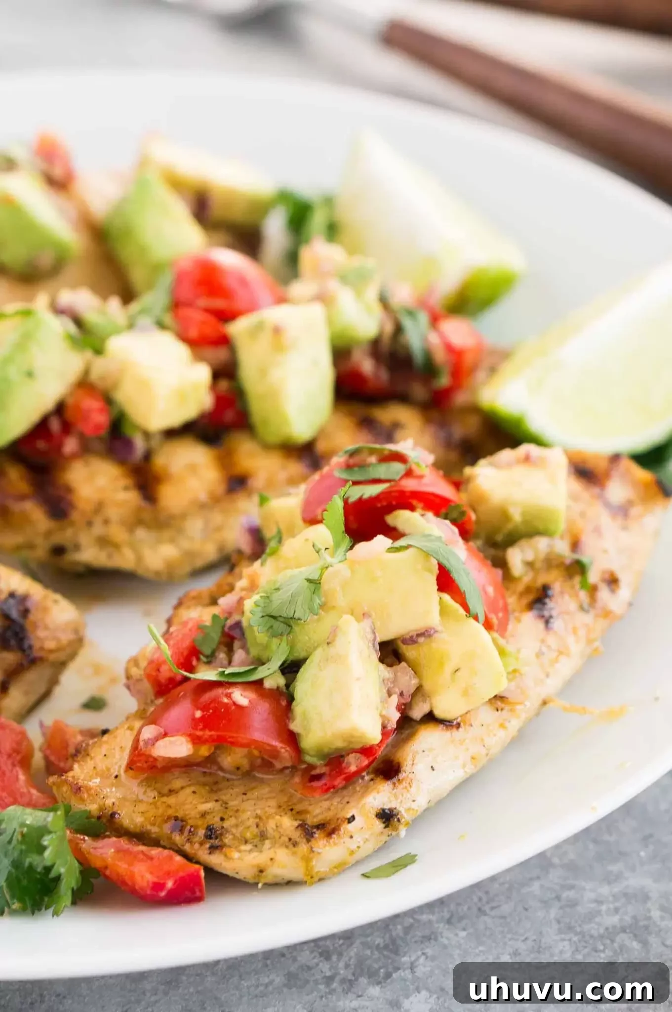 Platter of cilantro lime chicken topped generously with fresh avocado salsa, garnished with lime wedges and cilantro sprigs