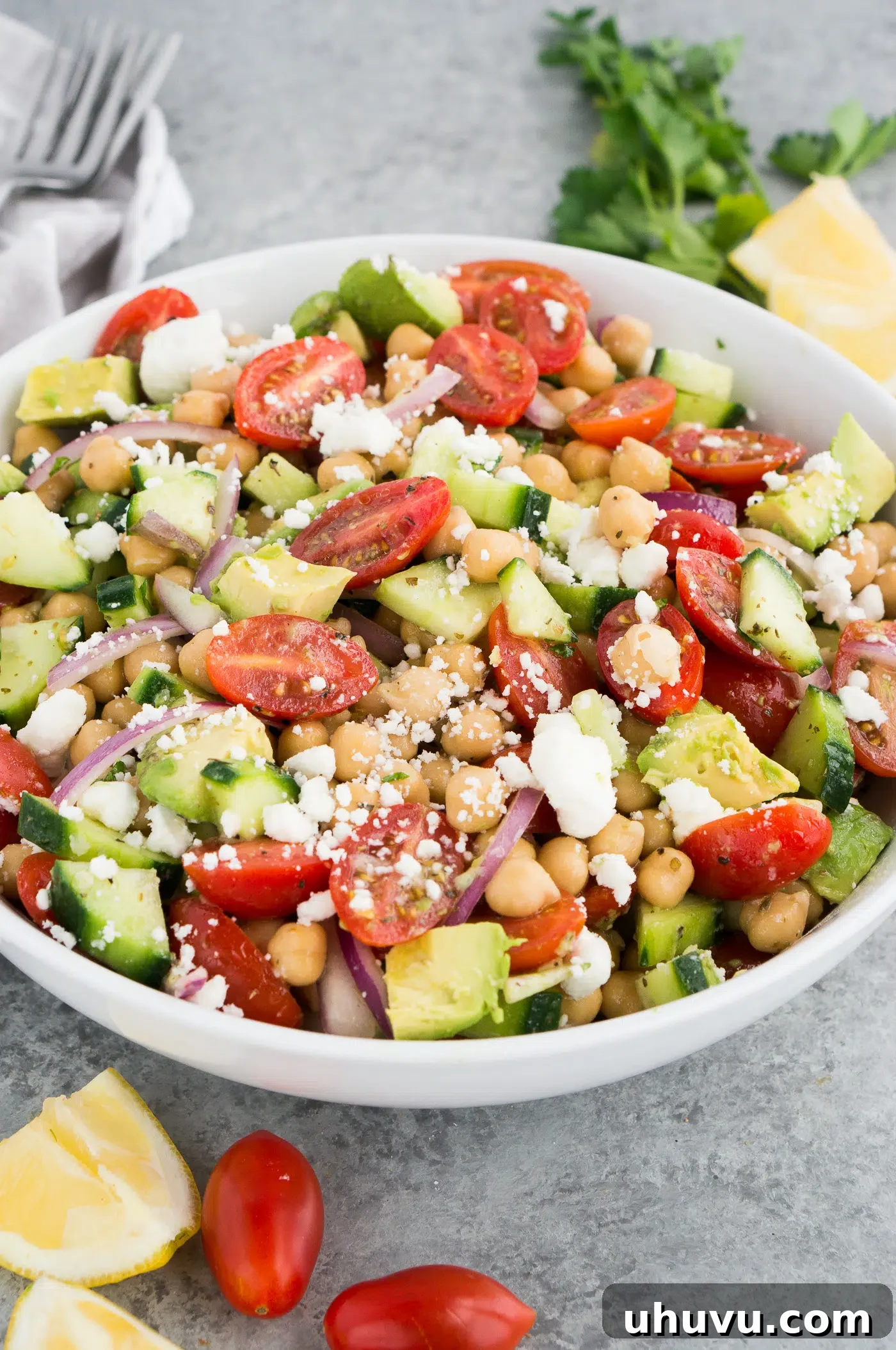 Close-up of a white bowl filled with healthy chickpea and avocado salad, garnished with fresh herbs.