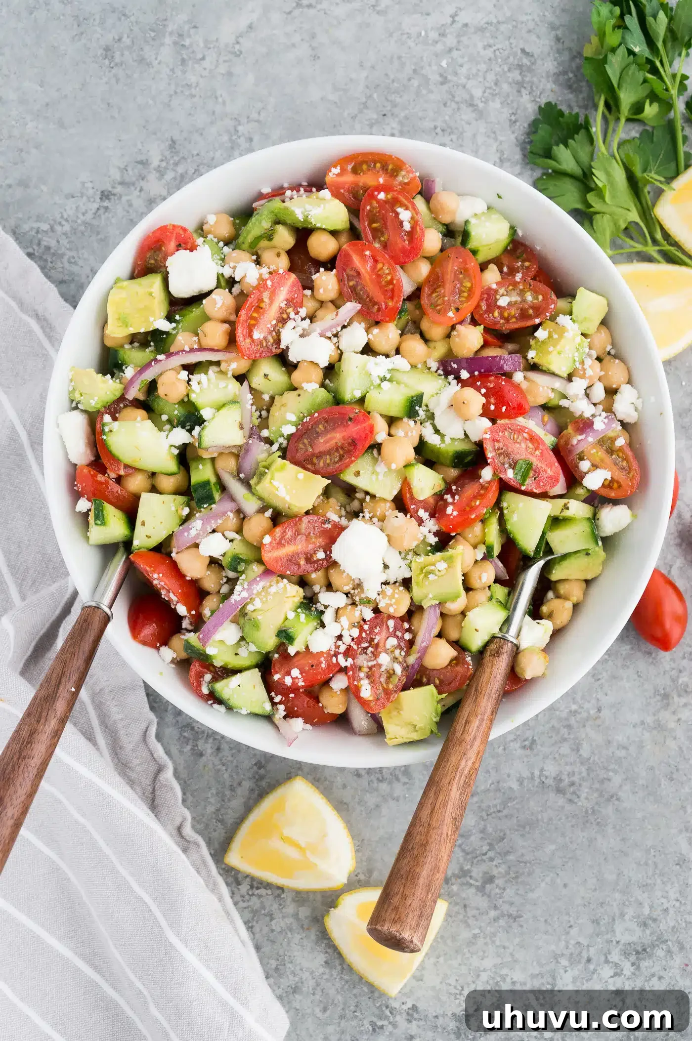 Chickpea and cucumber salad in a white bowl with salad tongs, perfect for serving at a gathering.