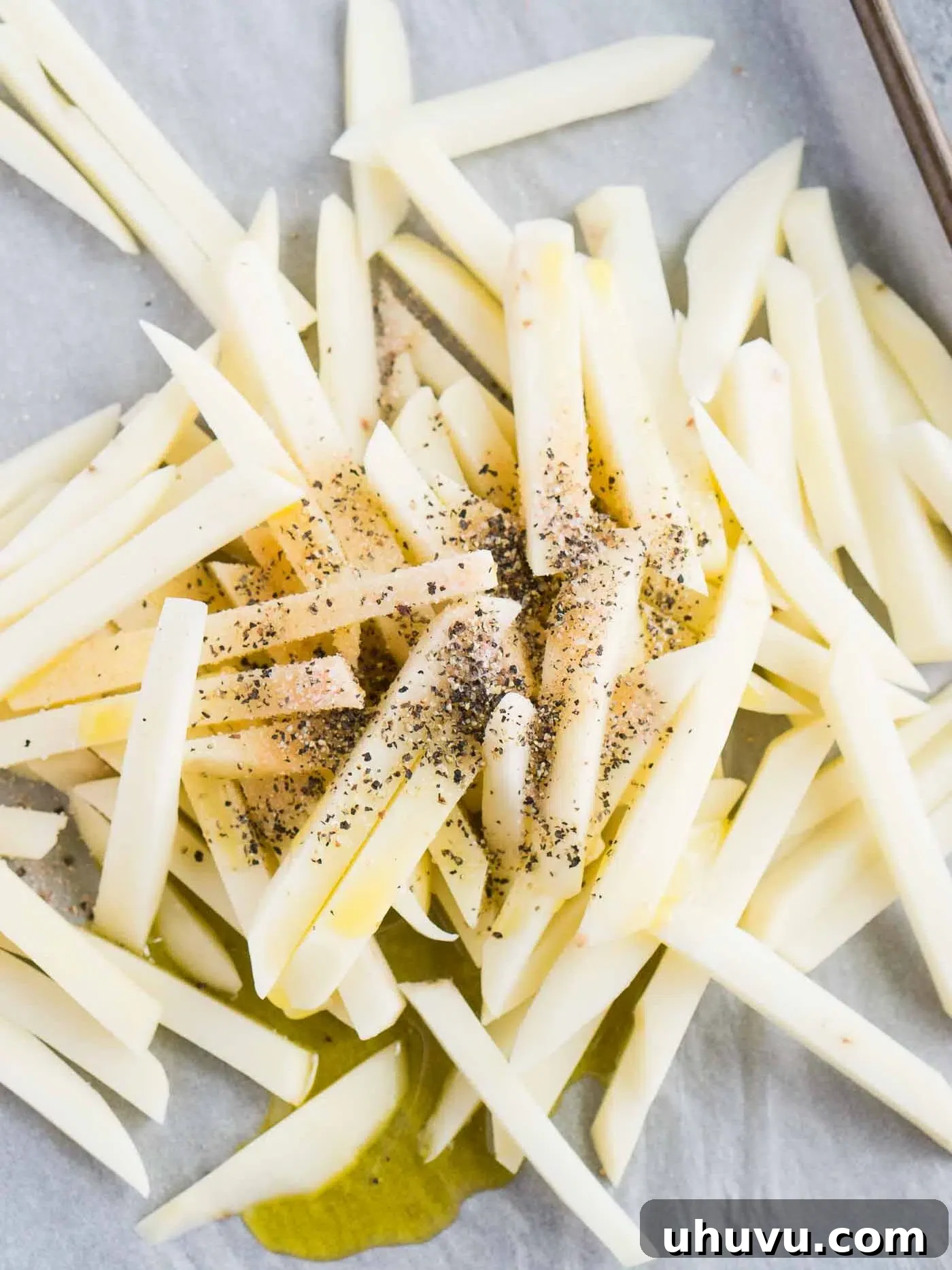 Seasoned potato fries spread on a baking sheet