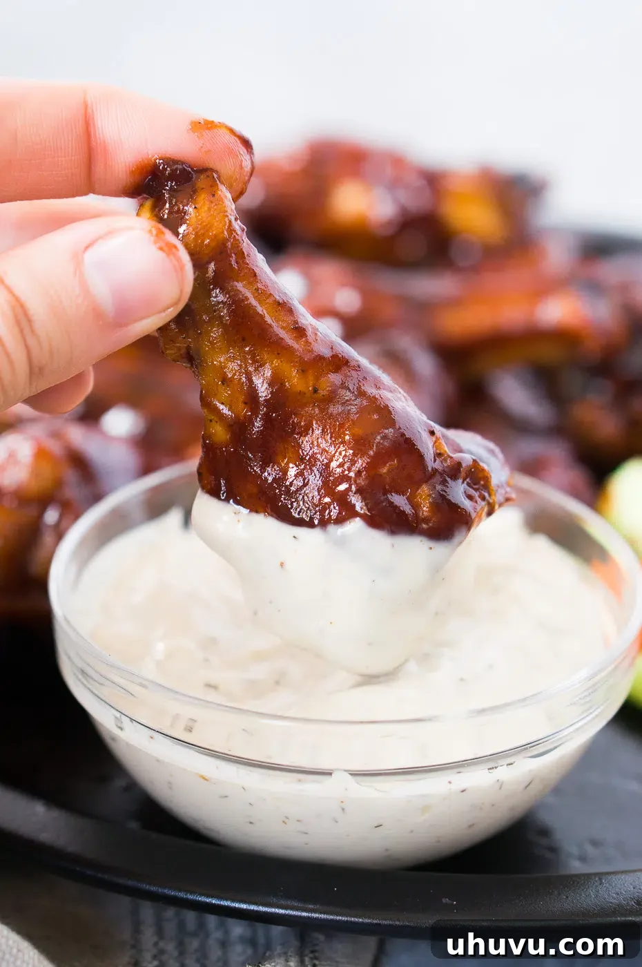 Close-up of a hand dipping a BBQ chicken wing in ranch sauce