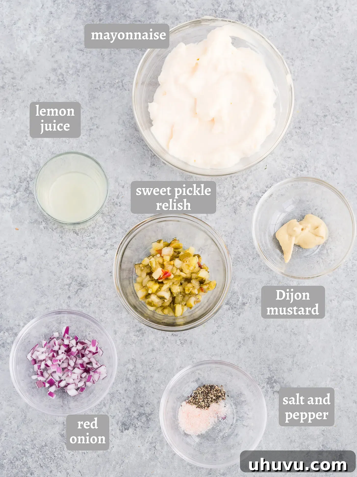 Individual ingredients for tartar sauce laid out on a table: mayonnaise, sweet pickle relish, minced red onion, lemon, and Dijon mustard.