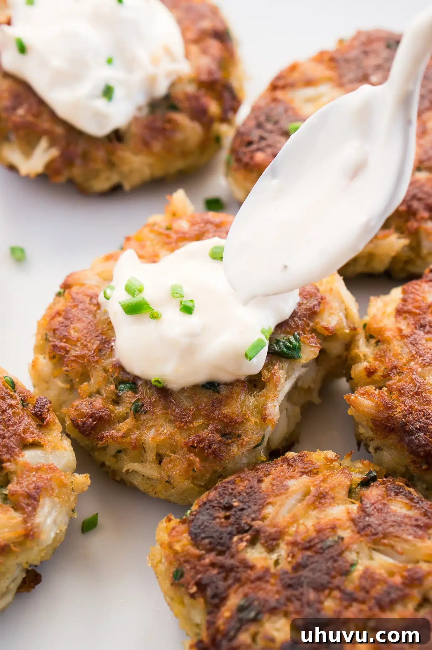 Two crab cakes topped with homemade tartar sauce on a serving plate.
