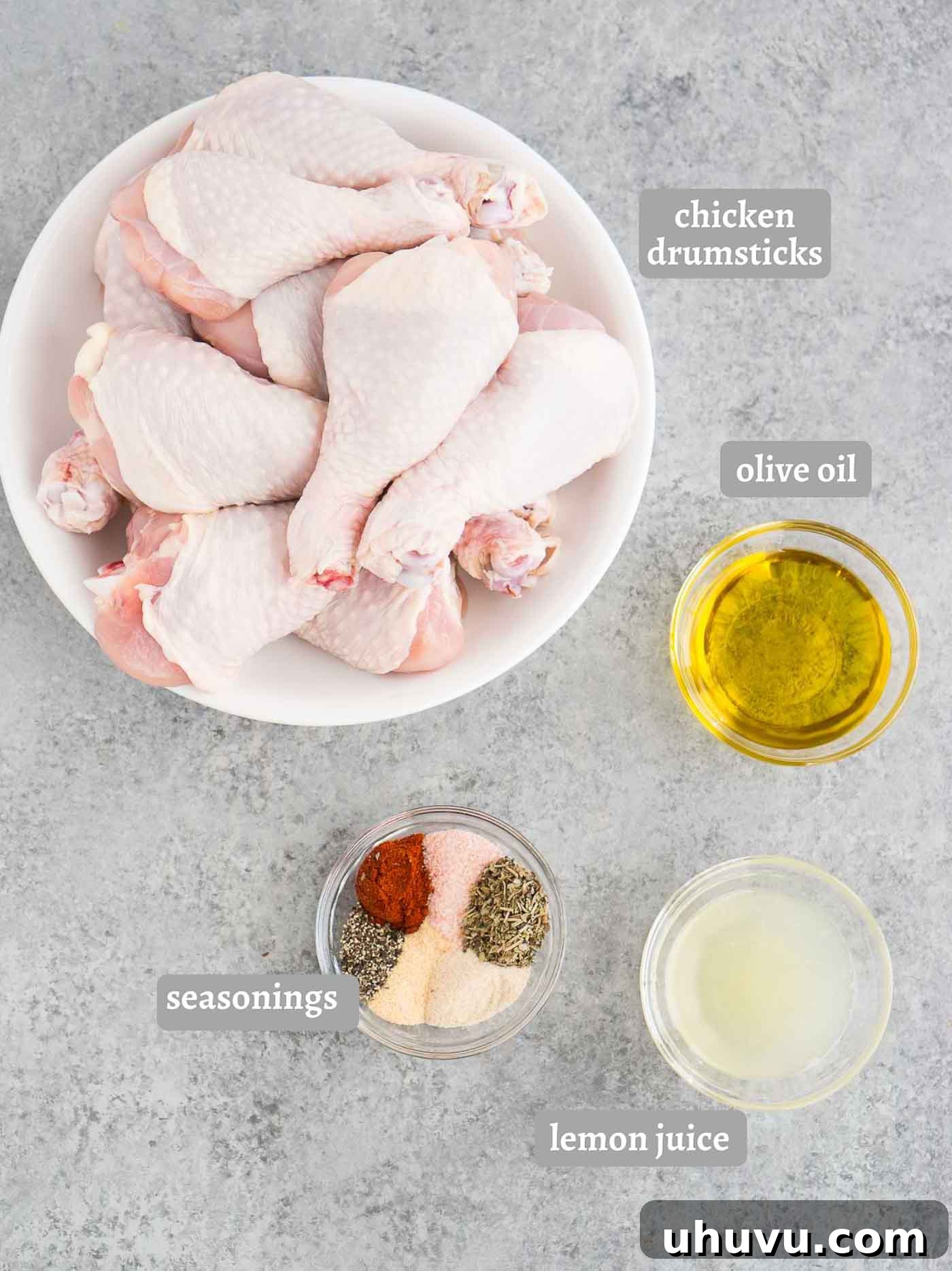 Crispy Baked Chicken Drumsticks 4 Ingredients for baked chicken drumsticks laid out: chicken legs, olive oil, lemon, and a selection of spices including paprika and Italian seasoning.