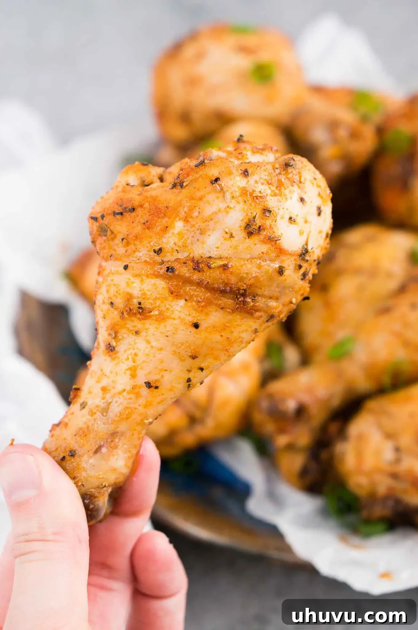 A hand holding a perfectly cooked, juicy oven baked chicken drumstick.