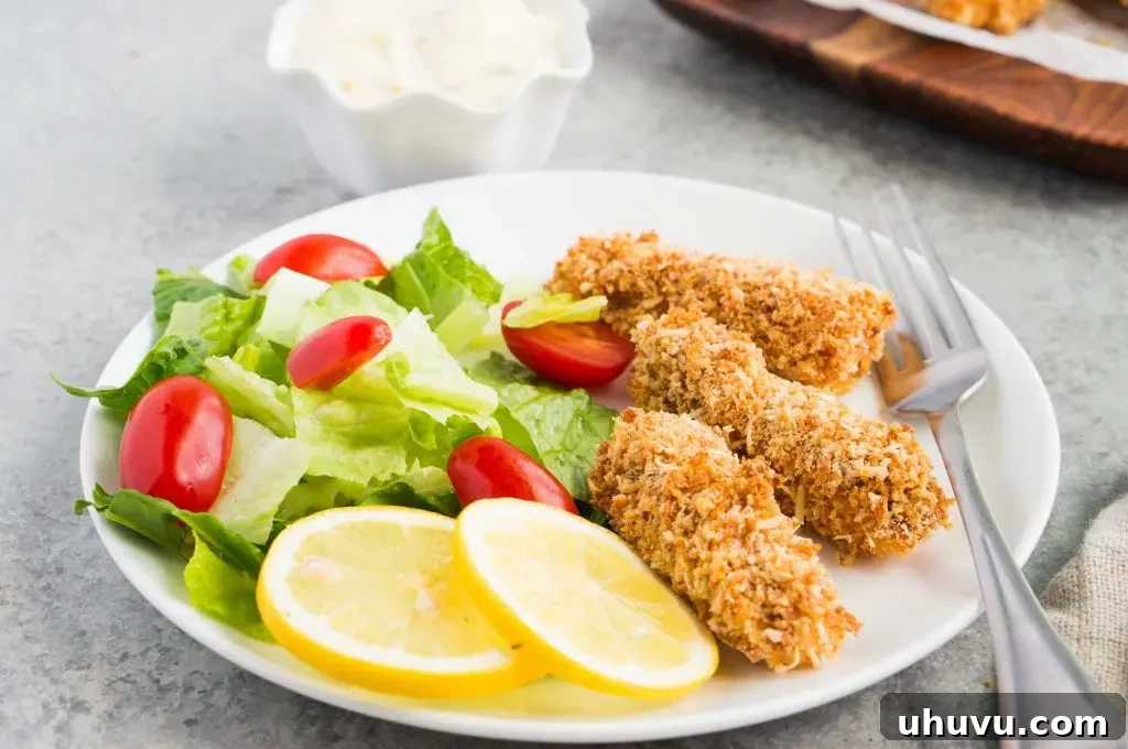 Plated baked fish fingers served alongside a vibrant green salad and fresh lemon slices, ready to be enjoyed.